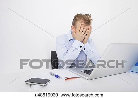 Tired businessman with hands on face sitting at desk by laptop View Large Photo Image Stock Image - Tired businessman with hands on face sitting at desk by laptop. Fotosearch