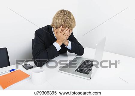 Tired businessman with hands on face sitting at desk by laptop View Large Photo Image Stock Photography - Tired businessman with hands on face sitting at desk by laptop. Fotosearch