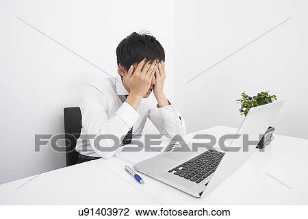 Stock Image - Tired businessman with laptop on desk in office. Fotosearch