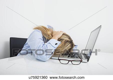 Stock Image - Tired businesswoman resting head on laptop in office. Fotosearch