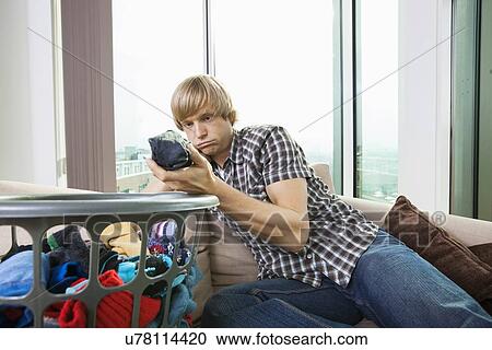 Stock Image - Tired man with laundry basket sitting on sofa at home. Fotosearch