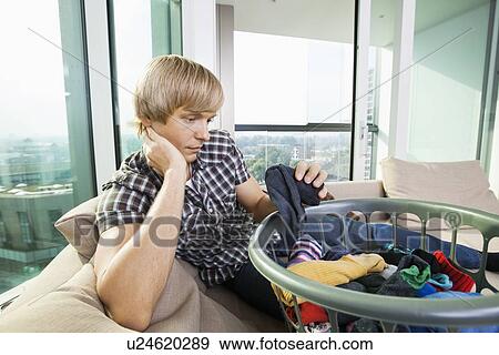 Tired man with laundry basket sitting on sofa at home View Large Photo Image Stock Photo - Tired man with laundry basket sitting on sofa at home. Fotosearch
