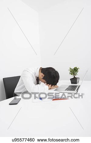 Stock Image - Tired mid adult businessman sleeping on desk in office. Fotosearch