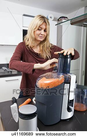 Woman juicing carrots at kitchen counter View Large Photo Image Stock Photo - Woman juicing carrots at kitchen counter. Fotosearch