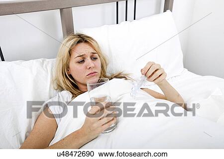 Woman suffering from cold holding water and tablet in bed View Large Photo Image Stock Image - Woman suffering from cold holding water and tablet in bed. Fotosearch