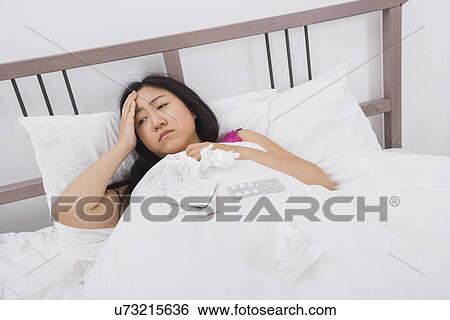 Stock Photograph - Woman suffering from headache and cold lying in bed. Fotosearch