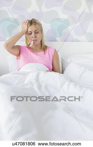 Woman taking temperature with thermometer while suffering from headache View Large Photo Image Stock Photograph - Woman taking temperature with thermometer while suffering from headache. Fotosearch