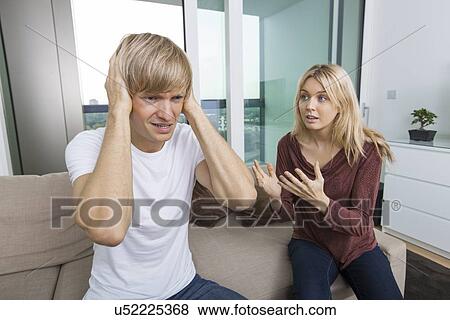 Woman trying to talk as man yells out aloud in living room at home View Large Photo Image Stock Photo - Woman trying to talk as man yells out aloud in living room at home. Fotosearch