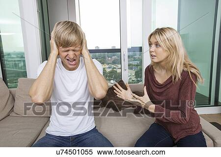 Woman trying to talk as man yells out aloud in living room at home View Large Photo Image Stock Photography - Woman trying to talk as man yells out aloud in living room at home. Fotosearch