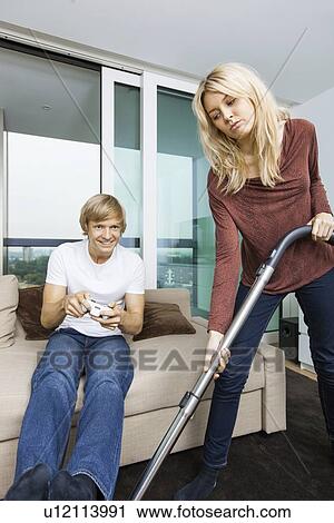 Woman vacuuming while man play video game in living room at home View Large Photo Image Stock Image - Woman vacuuming while man play video game in living room at home. Fotosearch