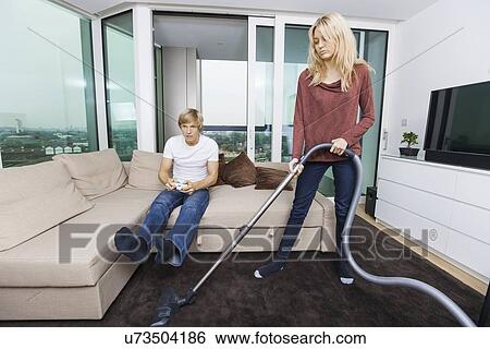 Woman vacuuming while man play video game in living room at home View Large Photo Image Stock Photograph - Woman vacuuming while man play video game in living room at home. Fotosearch