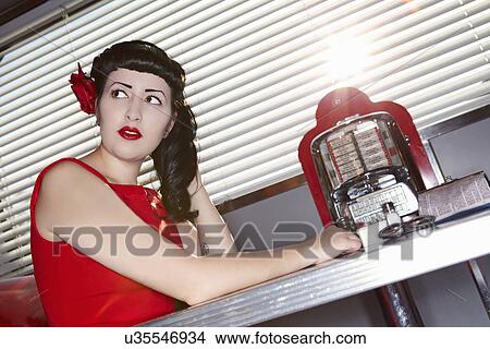 Picture - Young beautiful woman in red dress sitting at restaurant table. Fotosearch