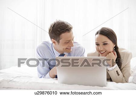 Stock Image - Young business couple using laptop in hotel room. Fotosearch