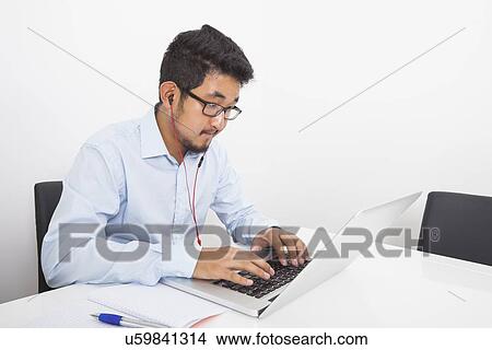 Young businessman listening music while using laptop in office View Large Photo Image Picture - Young businessman listening music while using laptop in office. Fotosearch