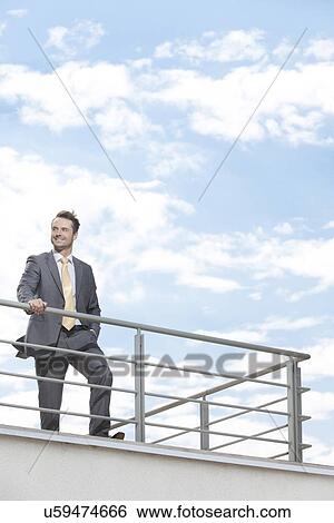 Young businessman standing at terrace railings against sky View Large Photo Image Stock Photograph - Young businessman standing at terrace railings against sky. Fotosearch