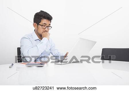 Stock Image - Young businessman working on laptop at desk in office. Fotosearch
