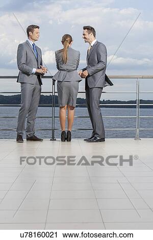 Stock Image - Young businesspeople standing at terrace railings against sky. Fotosearch