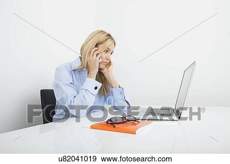 Stock Photo - Young businesswoman answering cell phone in office. Fotosearch