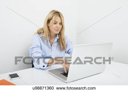 Stock Image - Young businesswoman using laptop at desk in office. Fotosearch