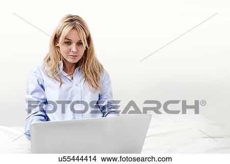 Picture - Young businesswoman using laptop in bed. Fotosearch