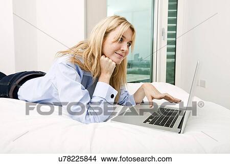 Young businesswoman using laptop while lying in bed View Large Photo Image Picture - Young businesswoman using laptop while lying in bed. Fotosearch