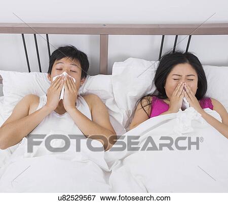 Young couple blowing noses in bed View Large Photo Image Stock Photo - Young couple blowing noses in bed. Fotosearch