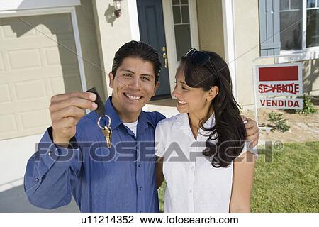 Stock Image - Young couple holding keys outside new home portrait. Fotosearch