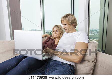 Stock Photo - Young couple using laptop in living room at home. Fotosearch