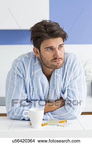 Young ill man with coffee mug and medicine leaning on kitchen counter View Large Photo Image Picture - Young ill man with coffee mug and medicine leaning on kitchen counter. Fotosearch