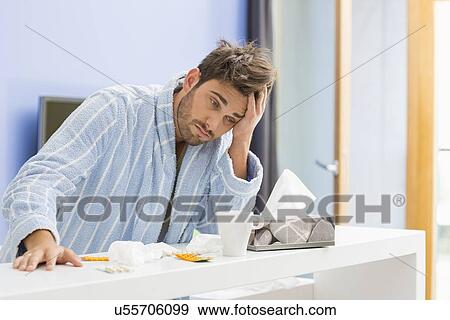 Young ill man with coffee mug, medicine and tissue leaning on kitchen counter View Large Photo Image Stock Photo - Young ill man with coffee mug, medicine and tissue leaning on kitchen counter. Fotosearch