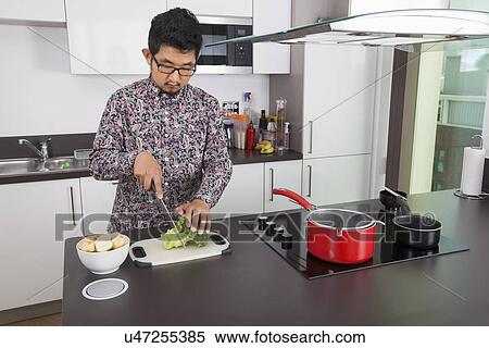 Young man chopping broccoli at kitchen counter View Large Photo Image Stock Photography - Young man chopping broccoli at kitchen counter. Fotosearch
