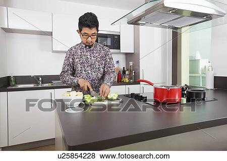 Stock Photo - Young man cutting broccoli at kitchen counter. Fotosearch