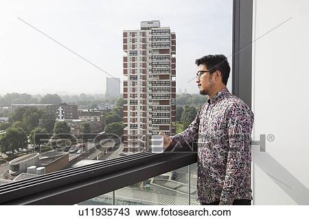Young man with coffee mug looking out through window at home View Large Photo Image Stock Image - Young man with coffee mug looking out through window at home. Fotosearch