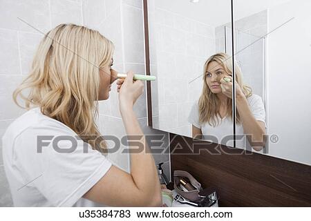 Young woman applying blush while looking at mirror in bathroom View Large Photo Image Stock Image - Young woman applying blush while looking at mirror in bathroom. Fotosearch