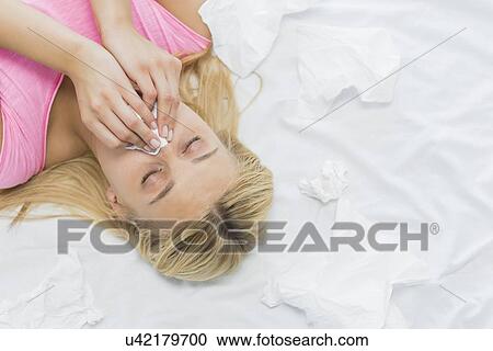 Young woman blowing nose in tissue paper while lying on bed View Large Photo Image Stock Image - Young woman blowing nose in tissue paper while lying on bed. Fotosearch