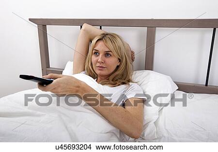 Young woman changing channels with remote control in bed View Large Photo Image Picture - Young woman changing channels with remote control in bed. Fotosearch