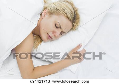 Stock Image - Young woman in pain lying on bed. Fotosearch