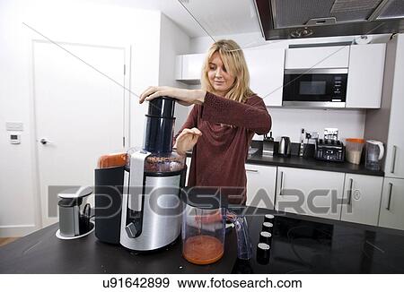 Stock Photo - Young woman juicing carrots at kitchen counter. Fotosearch