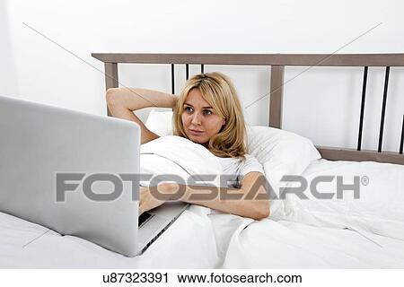 Stock Image - Young woman looking at laptop in bed. Fotosearch