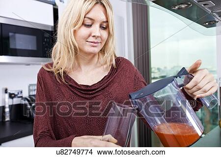 Picture - Young woman pouring carrot juice in glass at kitchen. Fotosearch