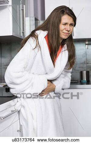 Young woman suffering from abdomen pain standing in kitchen View Large Photo Image Picture - Young woman suffering from abdomen pain standing in kitchen. Fotosearch