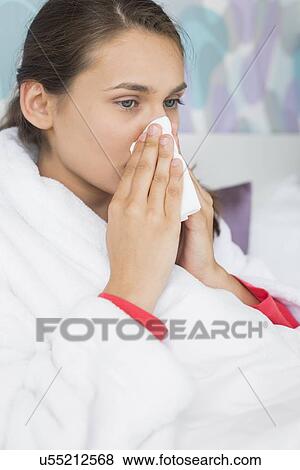 Young woman suffering from cold blowing nose in bedroom View Large Photo Image Stock Photo - Young woman suffering from cold blowing nose in bedroom. Fotosearch