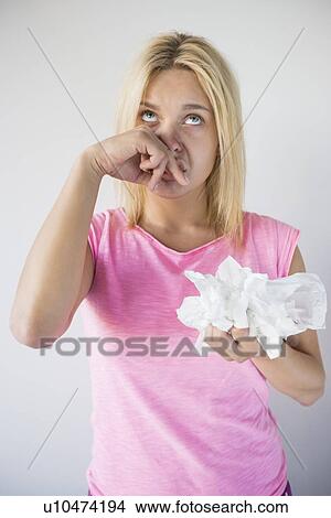 Young woman suffering from cold holding tissue papers against gray background View Large Photo Image Picture - Young woman suffering from cold holding tissue papers against gray background. Fotosearch