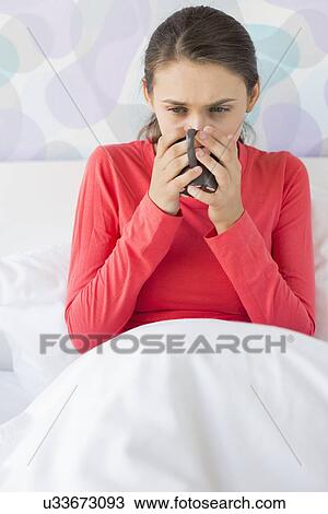 Stock Image - Young woman suffering from cold drinking coffee on bed. Fotosearch