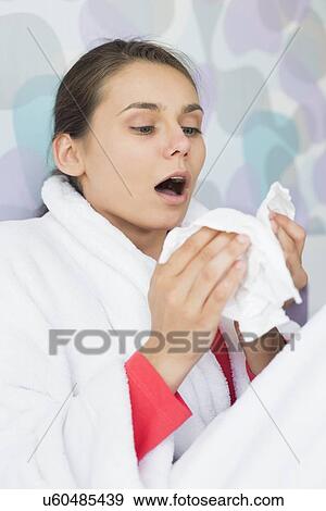 Stock Photo - Young woman suffering from cold sneezing at home. Fotosearch