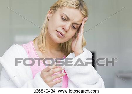Picture - Young woman suffering from headache while holding glass of water. Fotosearch