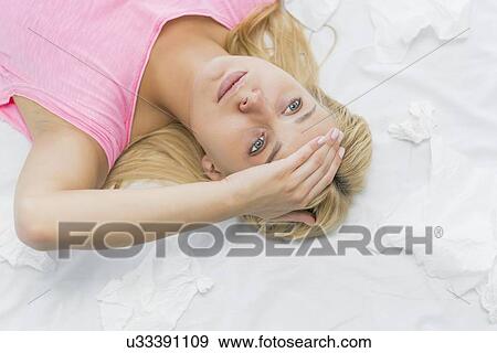 Stock Photo - Young woman suffering from headache while lying on bed. Fotosearch