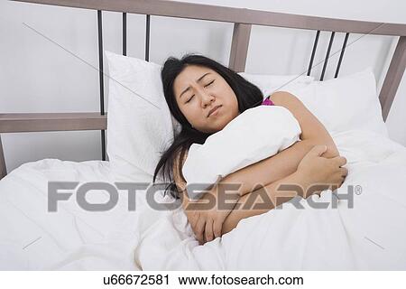 Stock Image - Young woman suffering from stomach ache lying in bed. Fotosearch