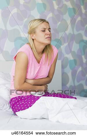 Picture - Young woman suffering from stomach pain in bedroom. Fotosearch