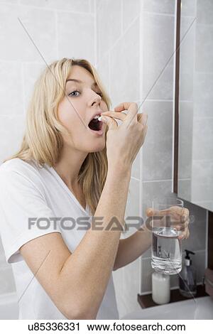 Stock Image - Young woman taking medicine in bathroom. Fotosearch